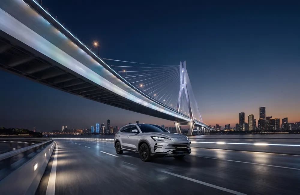 은색 BYD 씨라이언 6 DM-i가 해 질 무렵 사장교 아래 도로를 달리는 앞모습 측면 사진