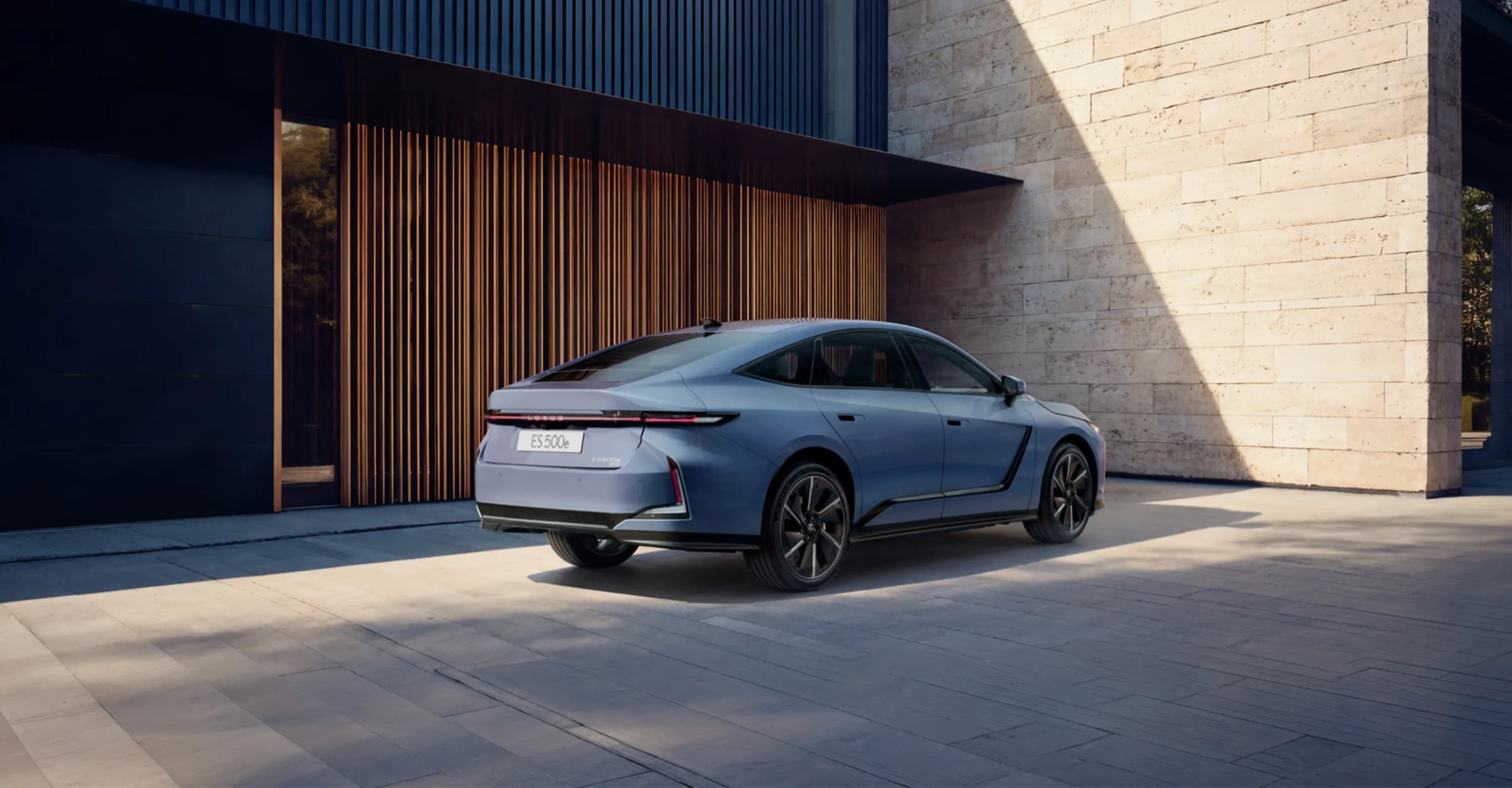 석조 건물 앞에 선 하늘색 렉서스 All-New ES 500e 후면. 차폭을 가로지르는 일자형 리어램프와 낮게 떨어지는 트렁크 라인이 보이는 렉서스코리아 공식 이미지