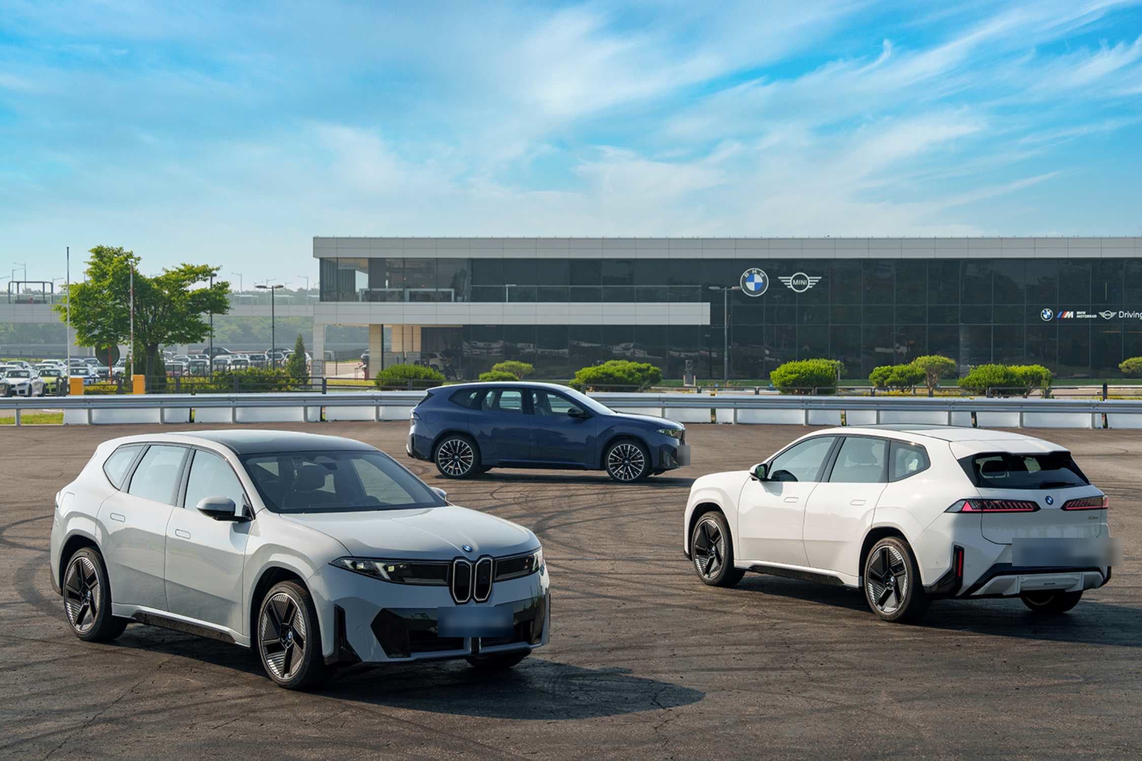 BMW 드라이빙 센터 앞 광장에 선 회색·남색·흰색 BMW iX3 세 대 (번호판 가림)