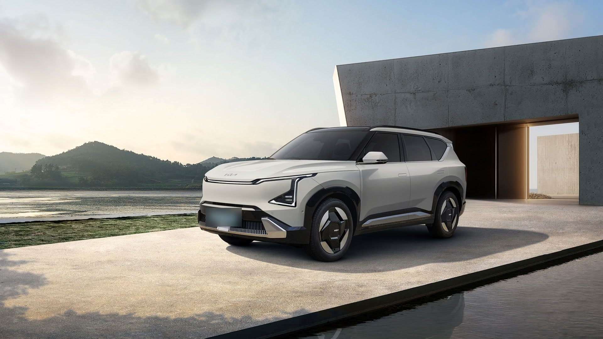 기아 EV5 흰색 앞모습, 바닷가 콘크리트 건물 앞에 서 있는 전기 SUV